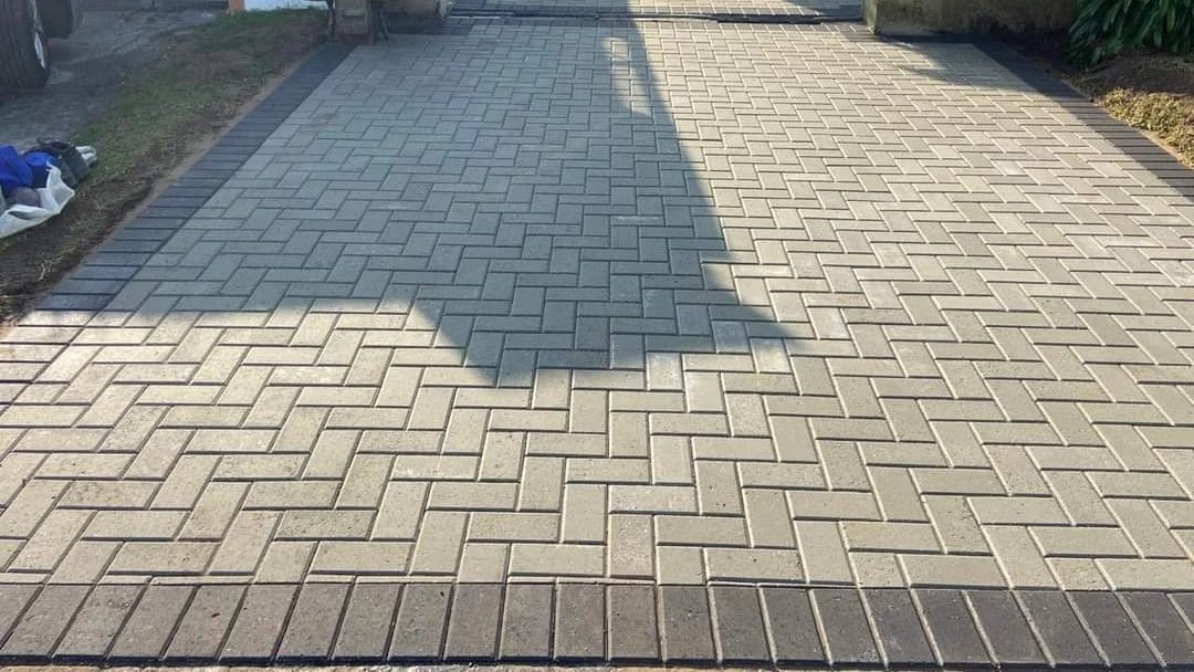 Herringbone driveway paving in buff pavers, edged with a charcoal paver border.