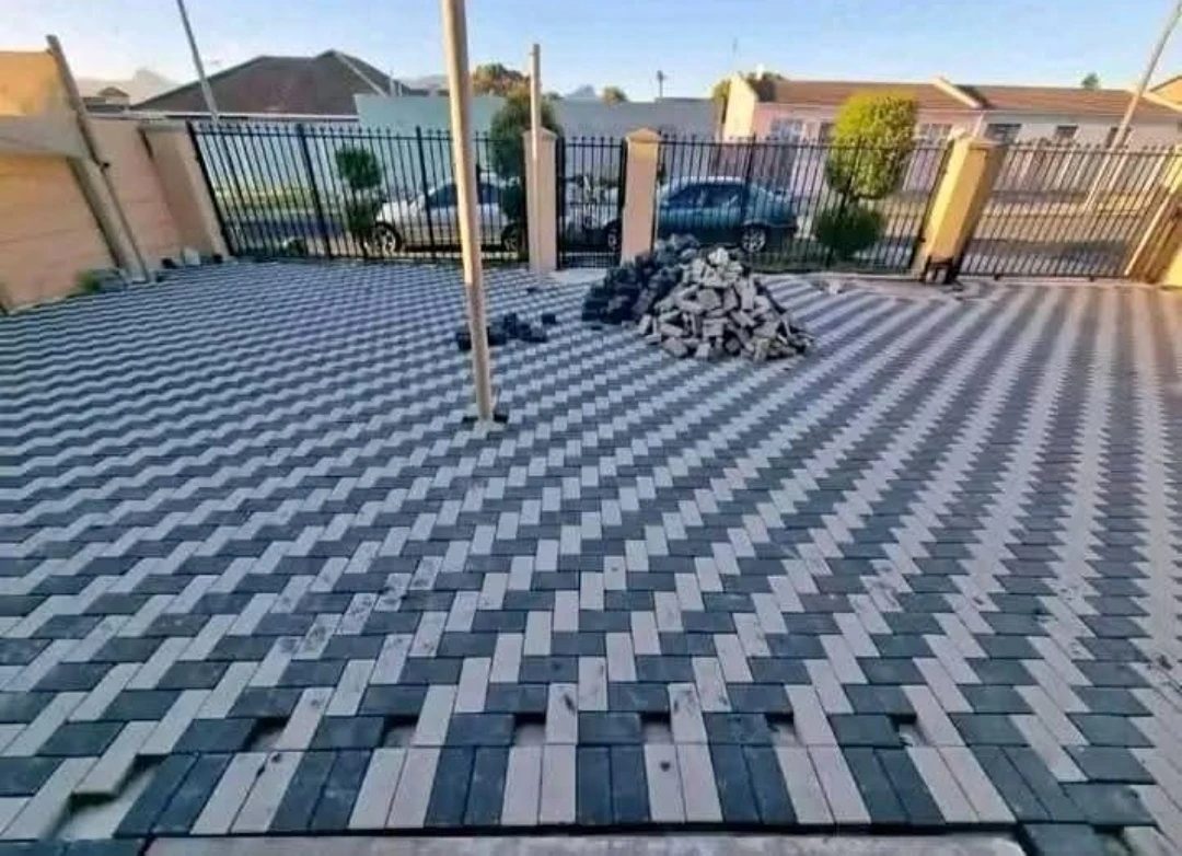 Charcoal and white herringbone paving mid-installation, with cut pavers stacked for the edges.