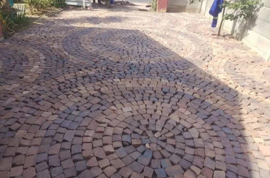 Cobblestone paving laid in overlapping fan-shaped arcs.