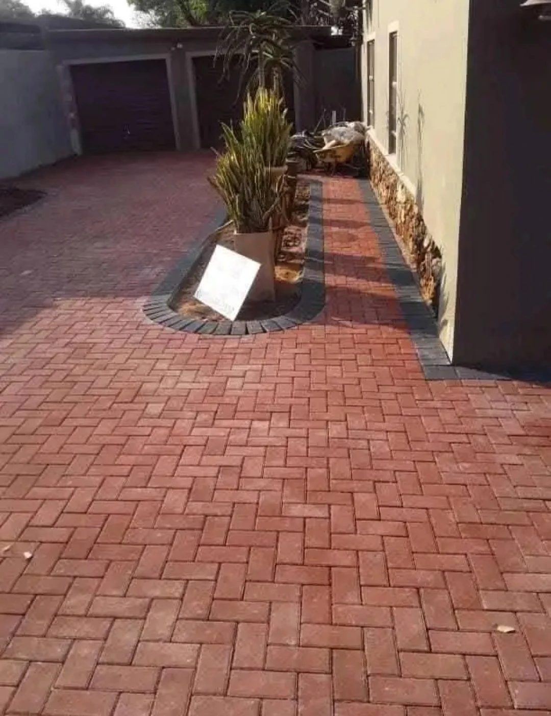 Red herringbone paving with a charcoal border curving around a planter bed.