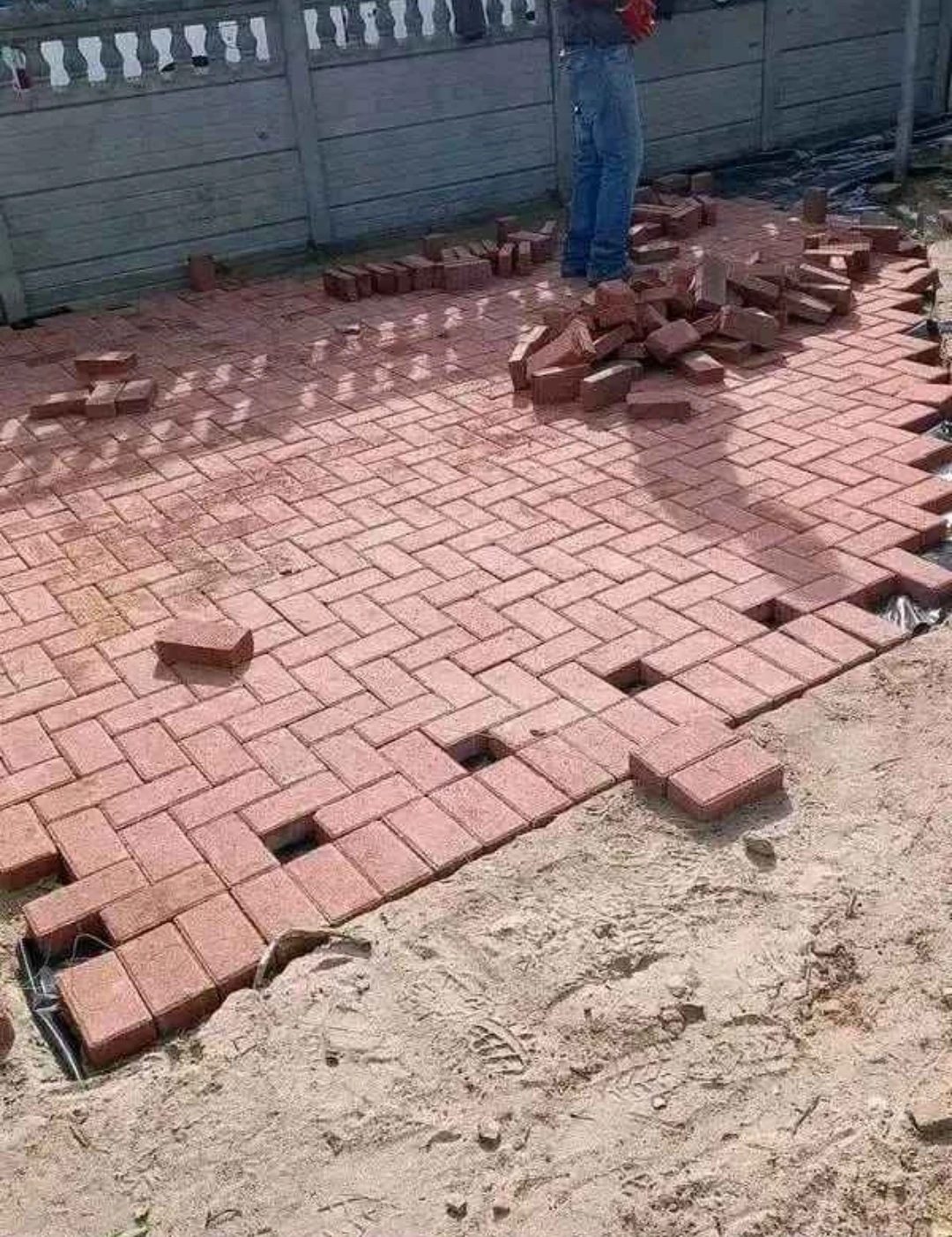Red pavers being laid in herringbone over levelled bedding sand.